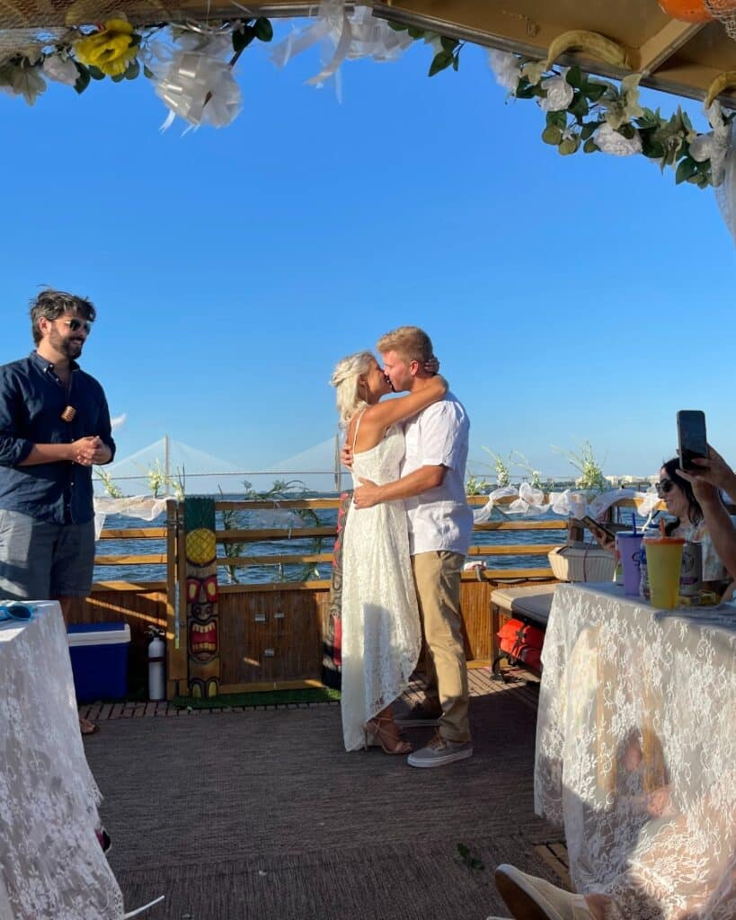Bride and groom sharing a kiss during a waterfront wedding ceremony aboard the Friki Tiki in Charleston.