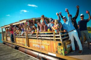Guests relaxing and enjoying a floating tiki bar experience on the Friki Tiki, featuring a tropical bar setup and premium sound system in Charleston.